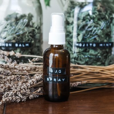 a homemade bottle of bug spray surrounded by herbs